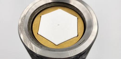 Early prototype thread protector: a white 3D printed hexagon fitted in a brass ring inside a steel cylinder
